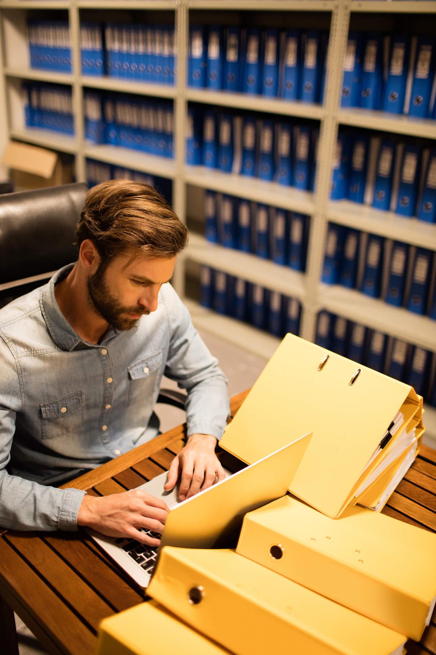 businessman-using-laptop-table-file-storage-room